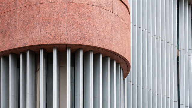 A close-up of a modern building facade featuring a curved red stone section and vertical metal slats, showcasing contemporary architectural design.