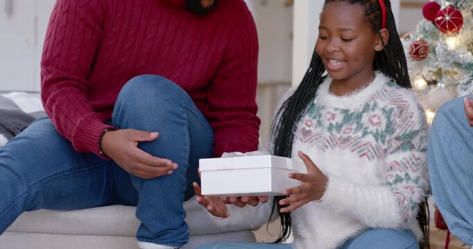 Family receiving white gift box from dad for holiday, opening and hugging on sofa by tree