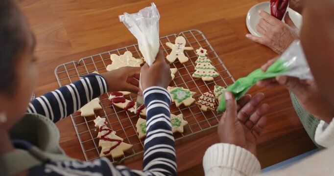 Family piping and decorating holiday cookies using piping bags on wooden table for celebration