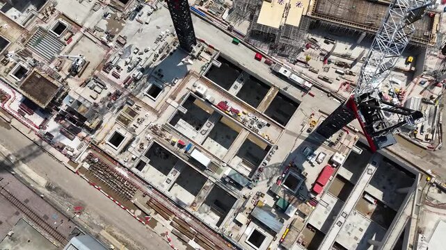 Top down view of deep concrete cells and structural walls of a station box under construction in west London, with a crawler crane working between the bays