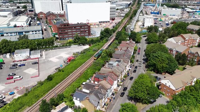Rows of terraced houses with long gardens back onto a railway line and industrial buildings in west London, seen from the air on a summer day