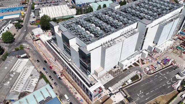 Aerial view of a large data centre with rows of rooftop cooling units in west London, surrounded by warehouses and construction work on an industrial estate