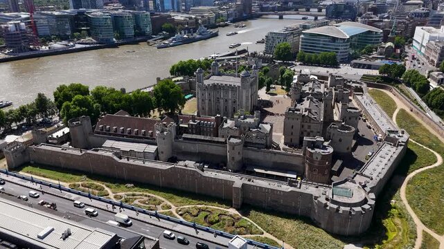 Aerial view of the Tower of London and its medieval curtain walls beside the river, with the White Tower at the centre and traffic passing on the road alongside