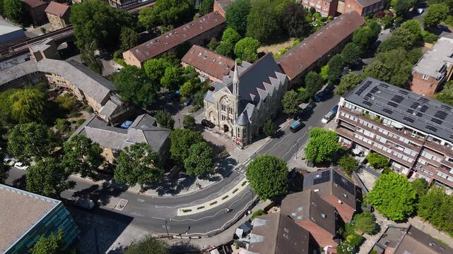 Red brick and stone church with a steep slate roof and rose window stands at a road junction among terraced housing