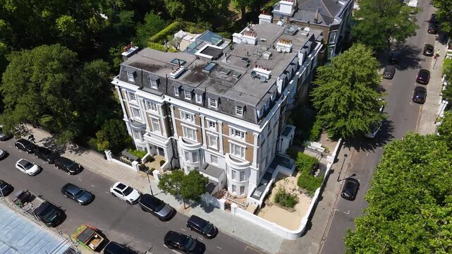 Grand white stucco corner mansion block with bay windows and balconies stands on a tree lined street of prime property