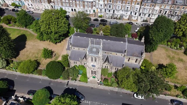 Victorian gothic church with a slate roof and pinnacled tower stands in its own leafy churchyard, framed by period terraces