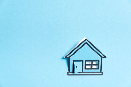 A minimalist blue miniature house model isolated on a light background, symbolizing homeownership, real estate, housing, property and residential architecture.