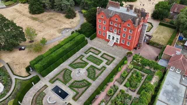 Red brick Jacobean palace stands behind a formal box parterre garden, with the surrounding parkland burnt brown