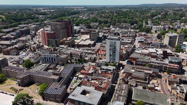 Wide view over the rooftops of a commuter town centre with a residential tower, car parks and shopping streets, with open countryside beyond