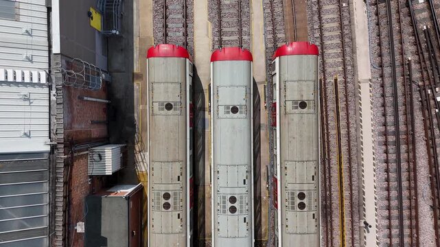 Three carriage roofs with red end domes run in parallel between the rails of a depot, seen from straight above