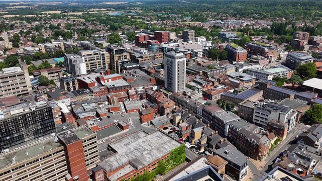 Aerial view across a commuter town centre showing shopping streets, offices, a residential tower and rooftops stretching to wooded countryside