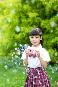 A young girl in a school uniform playing with bubbles outdoors