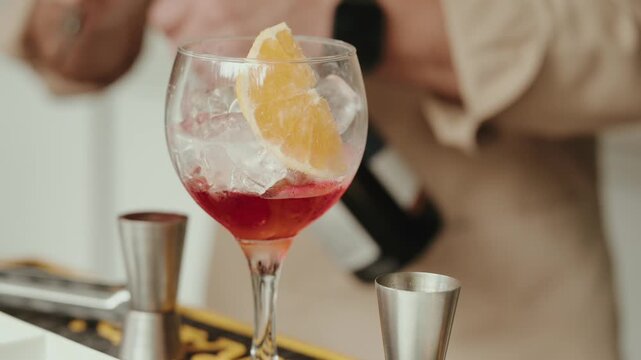 Balloon Glass Holding a Red Aperitif over Ice with an Orange Wedge beside a Steel Jigger