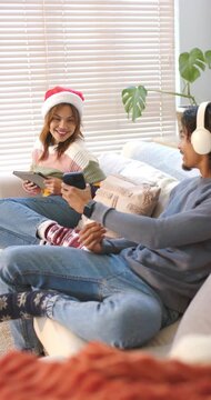 Vertical video: Diverse couple tapping smartphone and tablet to share clip while laughing on sofa