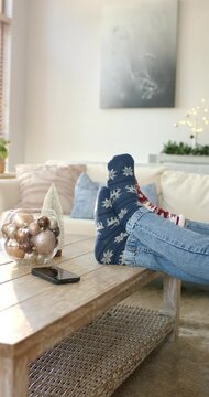 Vertical video: Legs sliding onto table with bowl of ornaments while flexing socks for holiday rest