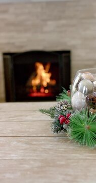 Vertical video: Burning logs flickering behind glass bowl holding baubles on table, creating glow