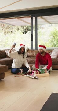 Vertical video: Couple sitting on floor by glass door filming on phone while wrapping holiday gifts
