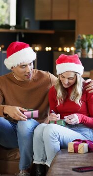 Vertical video: Couple sitting in living room with man pointing at gift box tag and woman writing