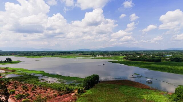 Views of Tra Tan in Lam Dong show a large lake surrounded by green fields. Cloudy skies highlight the area. Boats can be seen on the water as nature thrives in this location.