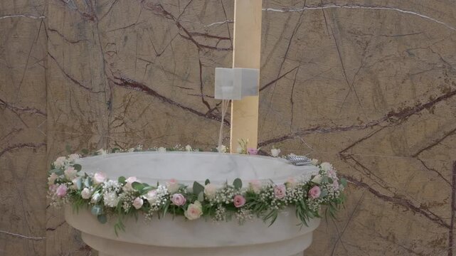 White Stone Baptism Font Edged With Pink Roses And Eucalyptus Against A Marble Wall