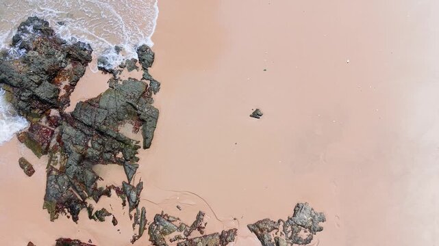 The camera captures different views of Ong Dia Rock Beach. Waves crash against the rocks and sand. People walk along the shore while enjoying the beachfront.
