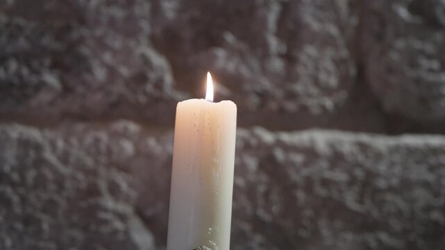 White Candle Flame Glowing In Front Of A Dark Textured Stone Wall