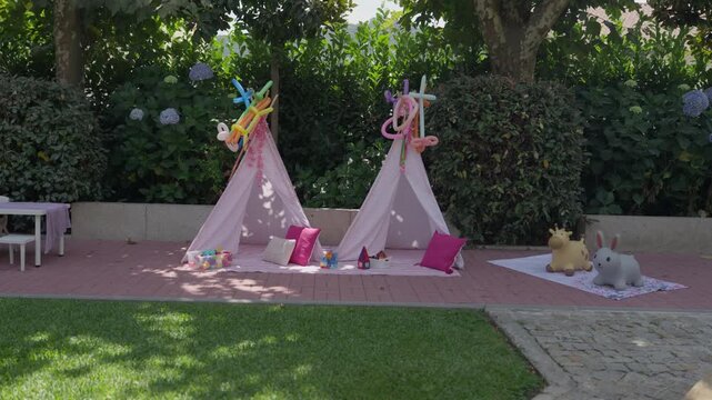 Two pink play tents with cushions and toys set up in a garden for a childrens party