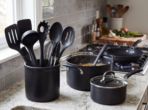 Black kitchen utensils arranged in a ceramic holder on a marble countertop with pots and pans cooking on a stove