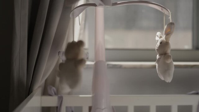 Soft bunny bear and star hanging from a baby cot mobile above a crib by a window