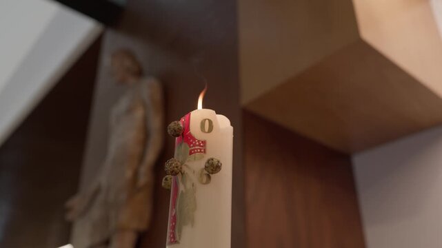 White pillar candle tied with a red ribbon and dried buds standing in a warm interior