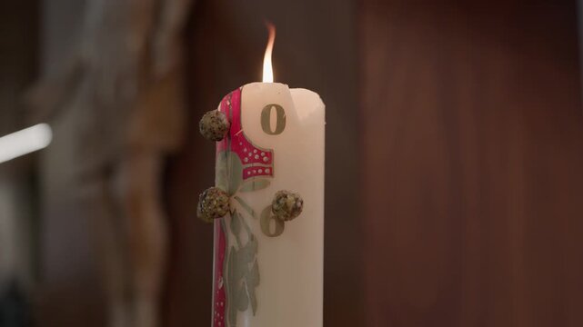 Flame burning on a white candle tied with a red ribbon and dried buds in a warm interior