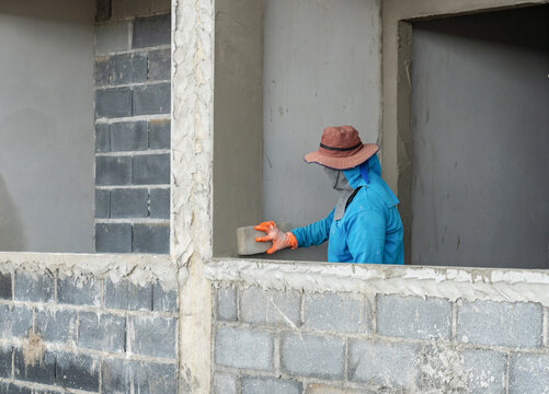 Construction worker smoothing a wet concrete plaster wall using a sponge float tool at a building development site.