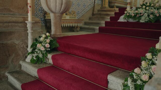 Pink and white rose arrangements lining red carpeted stone altar steps in a church