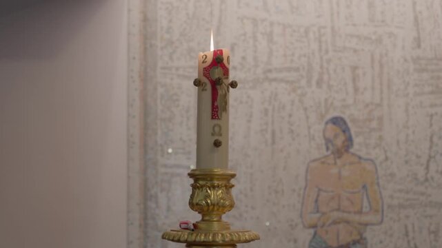 Burning paschal candle on a gilded candlestick in front of a pale church wall mosaic