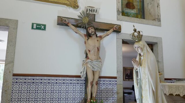 Church crucifix with silver halo beside Nossa Senhora de Fatima statue above azulejo tiles
