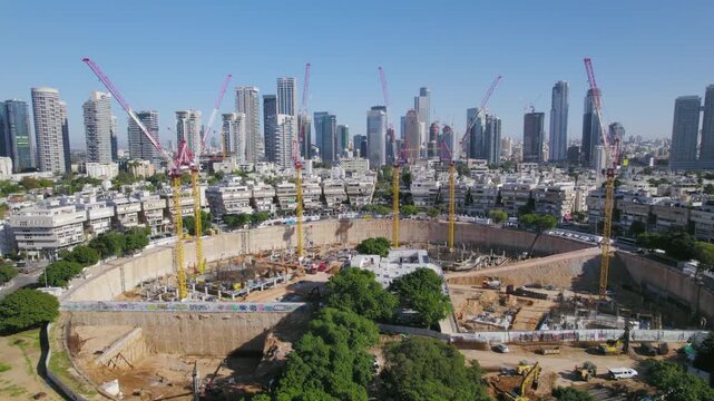 Aerial drone footage of massive construction site with multiple cranes and city skyline in background.