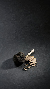 Whole black truffle with sliced pieces and a wooden truffle slicer on dark background
