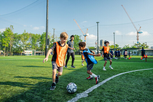 Group of diverse children practicing football on outdoor field with coach. 