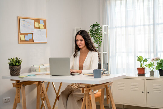 Hispanic young businesswoman typing on laptop while working from home. 