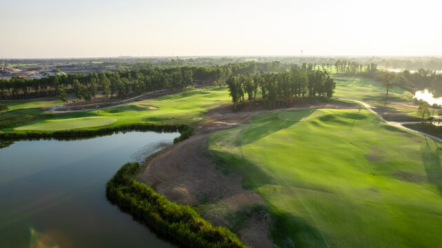 Aerial drone view flying over empty golf course near lake with lush greenery. 