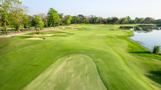 Flying drone view over a spacious empty golf course with green grass and rolling hills.