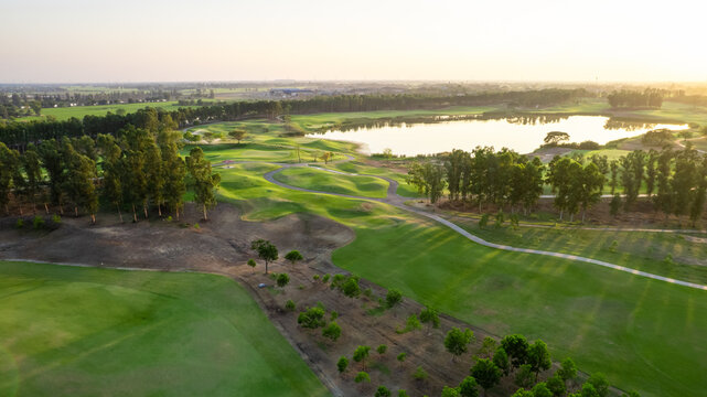 Aerial drone view flying over empty golf course near lake with lush greenery. 