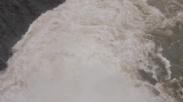 Powerful rushing water of waterfall cascading down from rock cliff into river.