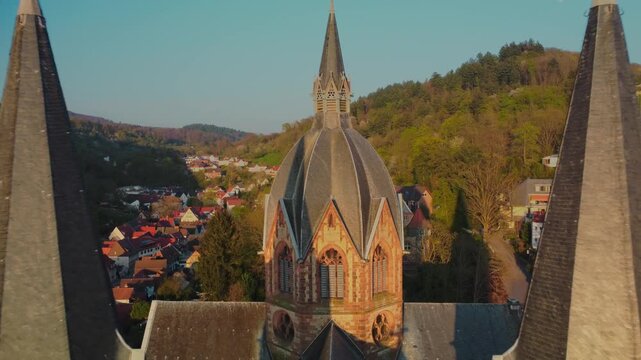 Aerial pull-out reveal shot from St. Peter's Cathedral spires showing historic Heppenheim town at golden sunset, Germany