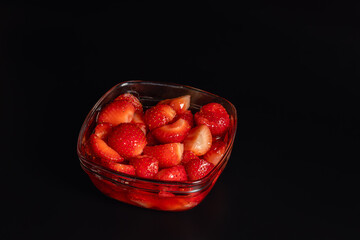 High angle view of fresh sliced ripe strawberries in sweet syrup filled in a square glass bowl isolated on black background with copy space on top right © Ol-Ni