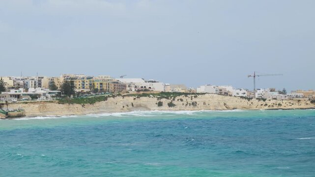 coastal town skyline apartment buildings limestone bluff turquoise bay construction crane mediterranean architecture malta coastline overcast day aerial view