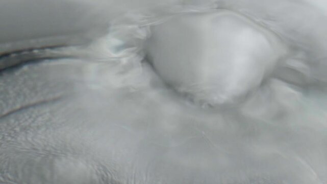 Close up of water droplet creating circular ripples on smooth water surface, showing gentle waves, reflections and soft flowing movement in an abstract scene