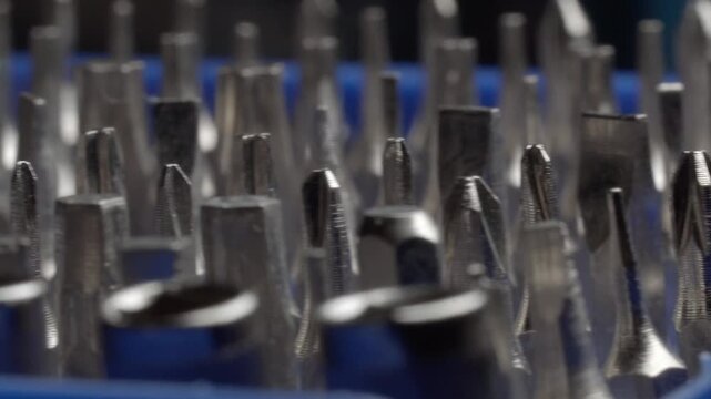 Close up of metal drill bits arranged together, showing sharp tips, textured surfaces and blue bases with shallow focus highlighting industrial tools and detailed craftsmanship