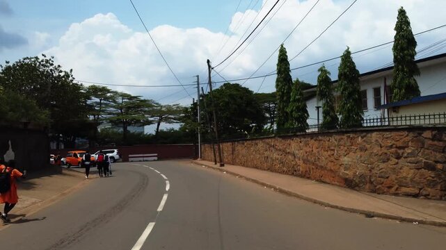 Pedestrian commute on residential street near school building in African city.