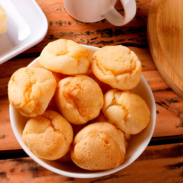 Homemade Brazilian cheese bread served on a wooden platter, accompanied by fresh Minas cheese, butter, and black coffee